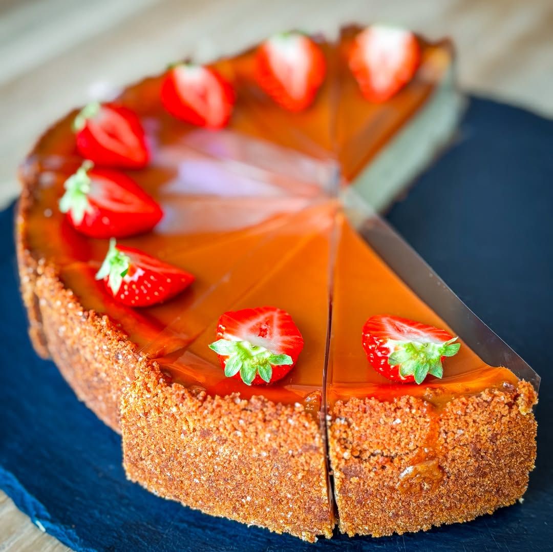 Nakrájený cheesecake na sušenkovém korpusu s karamelovou polevou a jahodami